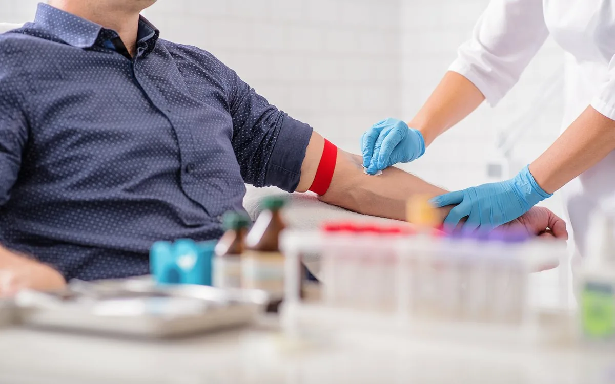 Coleta de sangue com garrote no braço e tubos de amostra sobre a bancada